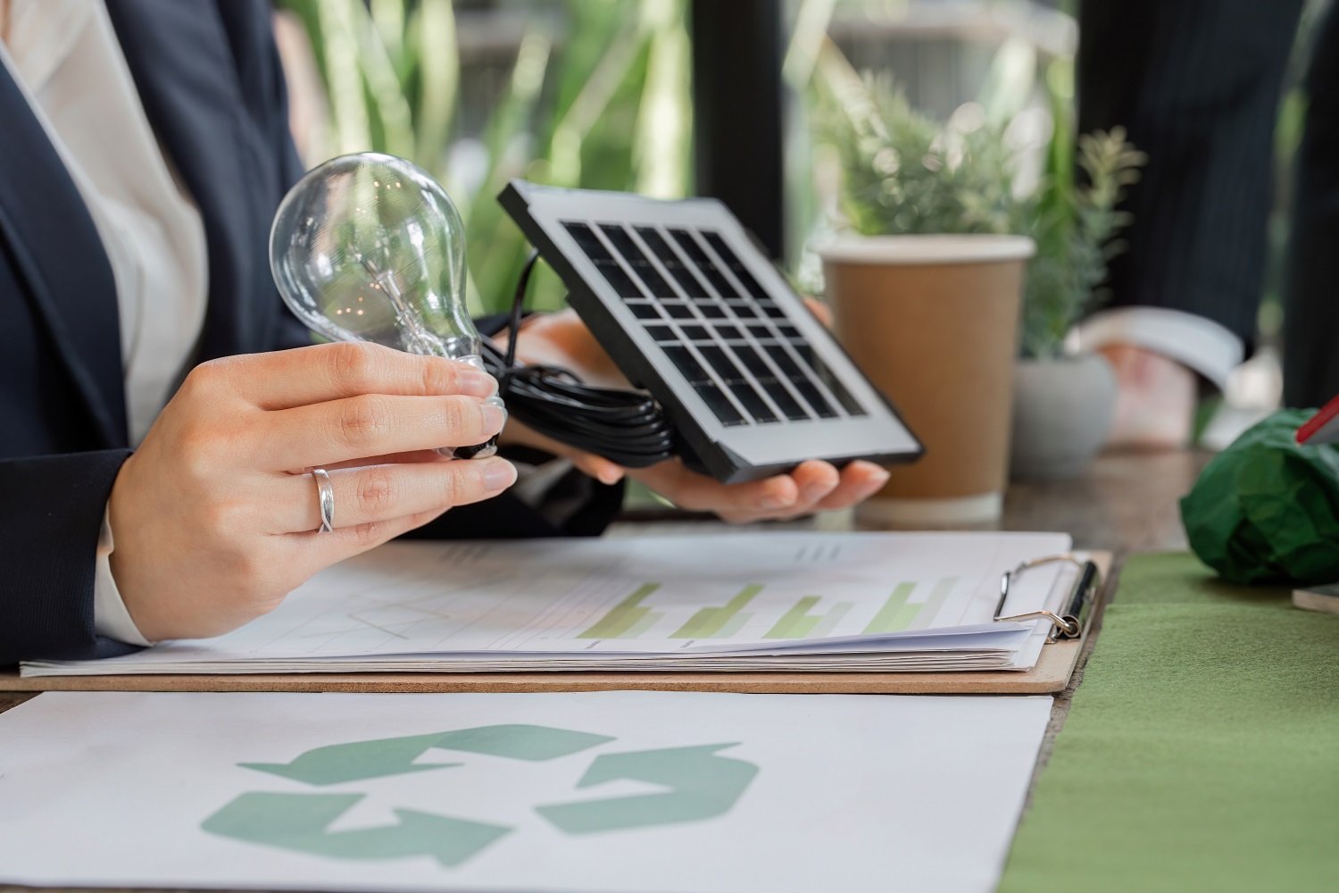 A businessperson holds a solar panel and an LED bulb, focusing on innovative green technologies to enhance energy savings and promote eco-conscious decisions within an organization.